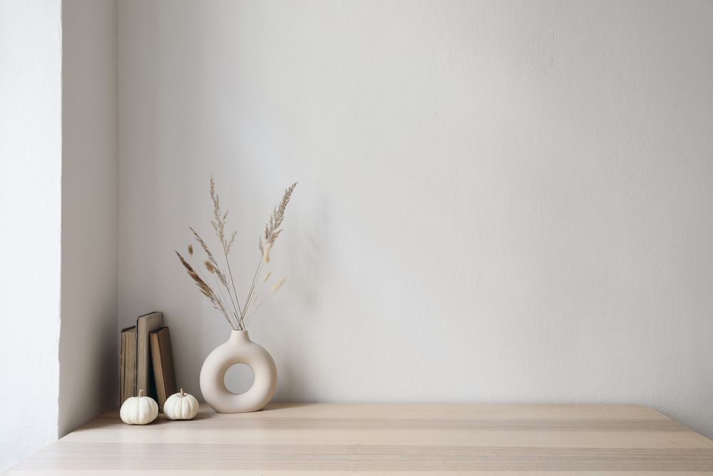 Elegant moody Scandinavian interior with vase and dry grass bouquet, old books and little mini pumpkins