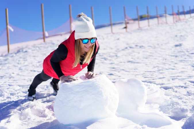 Happy female in winter gear doing a plank on a big ball of snow outside