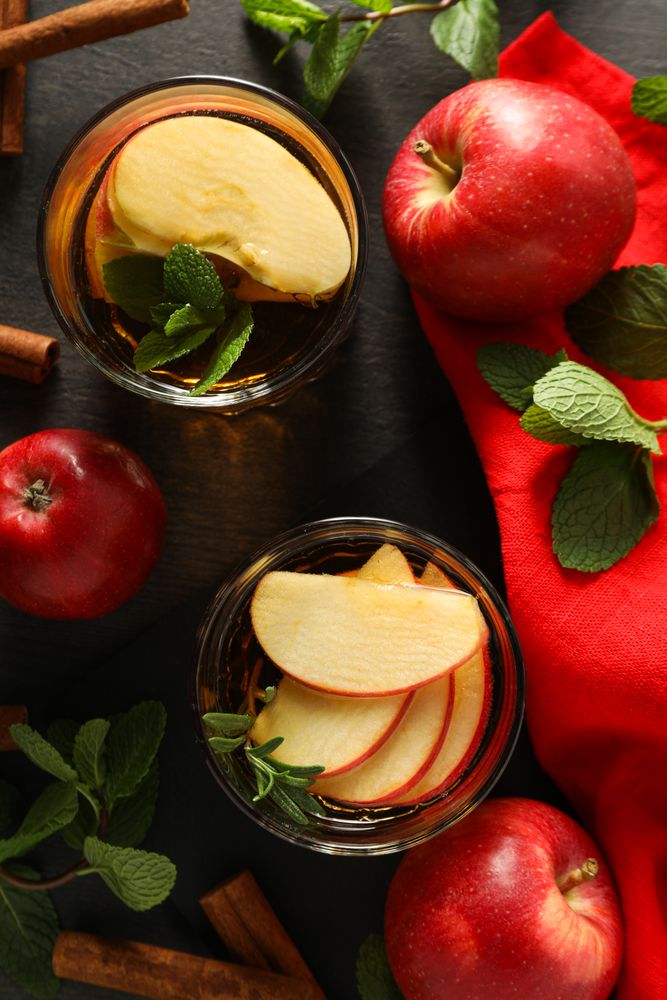 Glasses with apple cider, mint leaves and red apples on dark wooden background, top view