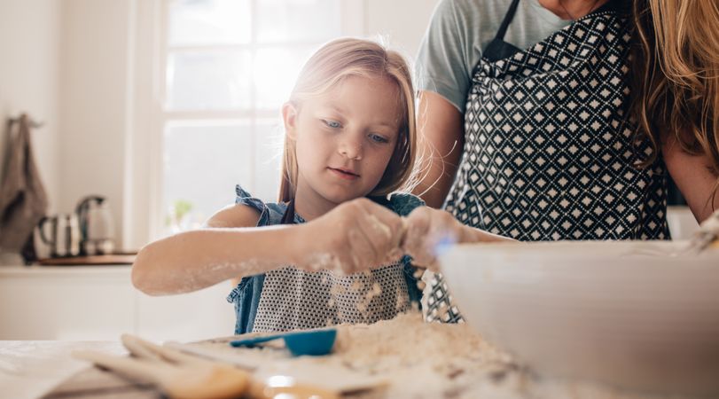 Young girl cooking with flour in the kitchen with her mother