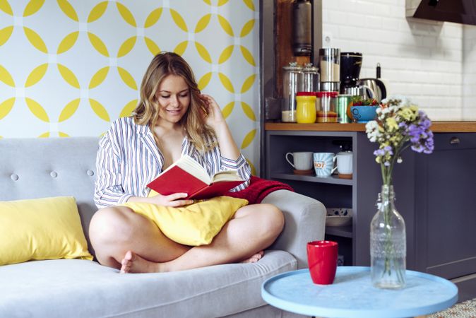 Young happy female reading book on sofa