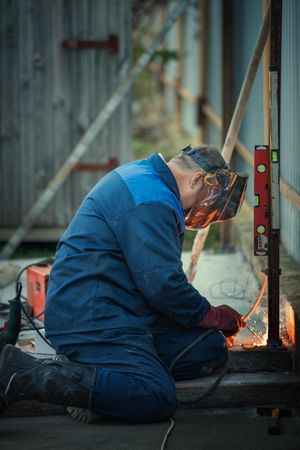 Man in blue uniform and goggled welding a rod outdoor