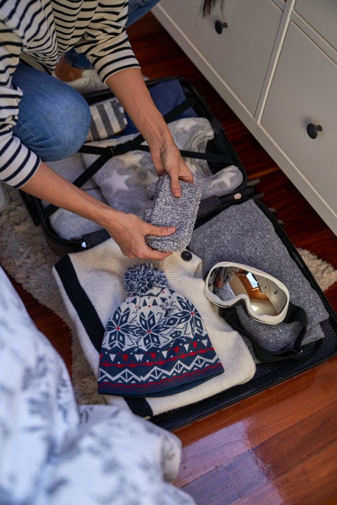 Crop tourist putting socks unto full luggage on floor