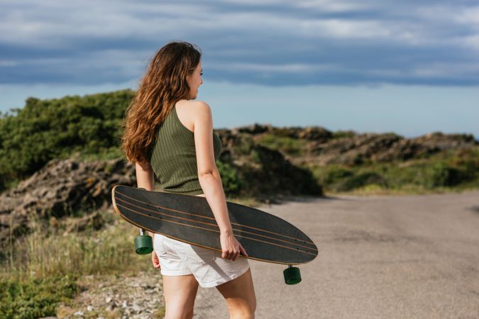 Anonymous skater with longboard walking on pavement against mount