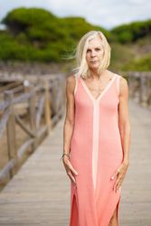 Austere older woman with grey hair on wooden walkway near the coast, vertical