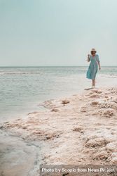 Woman in blue dress and a hat standing on seashore 5ryZ30