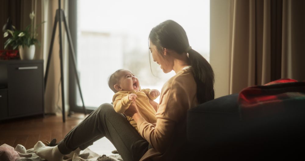 Mother and Baby Bonding Moment: Authentic Shot of an Asian Woman New to Motherhood Playing with her Cute Child in the Morning at Home.