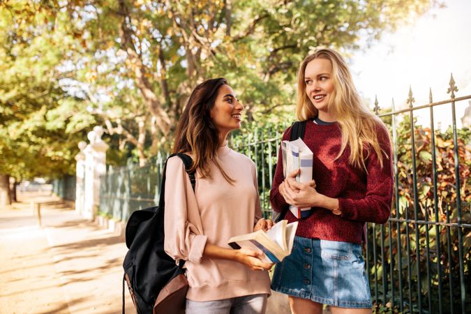 Happy female students holding books and talking after class outdoors