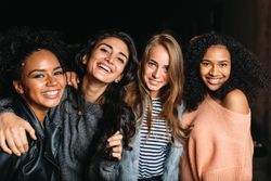 Multi-ethnic group of smiling women embracing outside at night