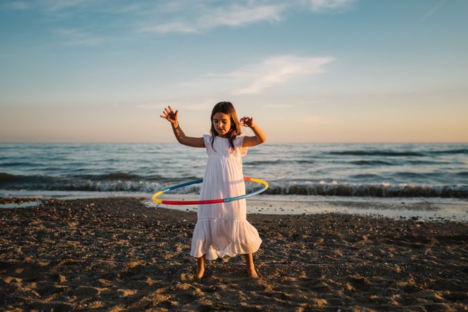 Adorable girl playing with hula hoop ribbon on seaside