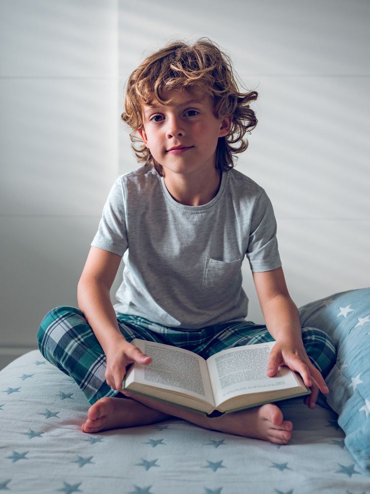 Cute boy sitting on bed with opened book
