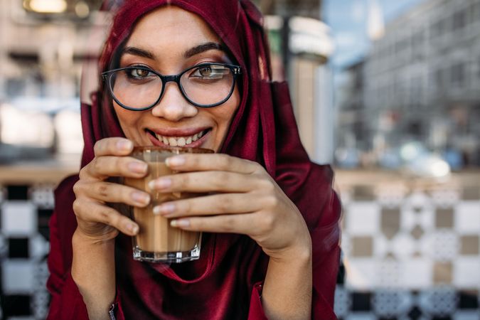 Close up portrait of smiling Muslim woman wearing eyeglasses drinking coffe