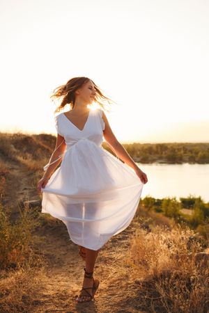 Blonde female in ethereal summer dress walking away from lake