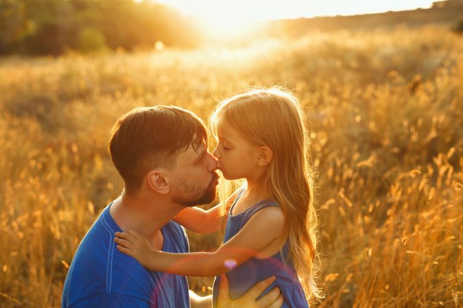 Female child kisses her father in field at sunset