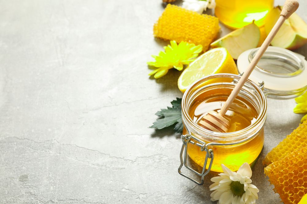 Honey, flowers and fruits on grey background, copy space