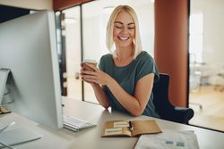 Blonde businesswoman smiling and holding a coffee at her work computer