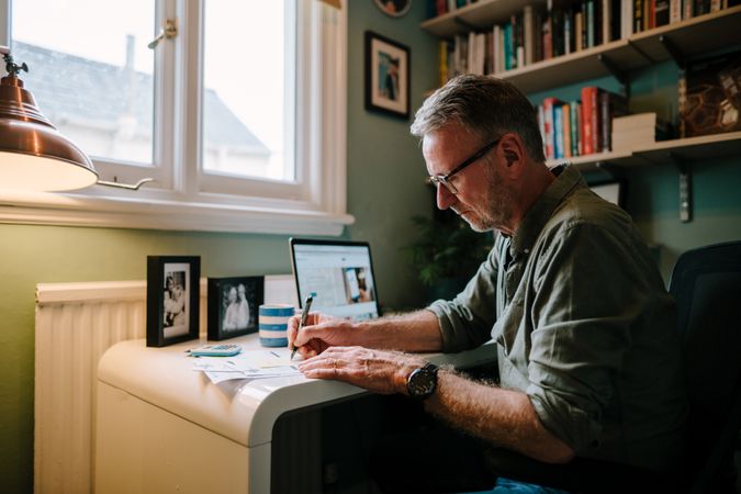 Older man writing notes in cozy home office