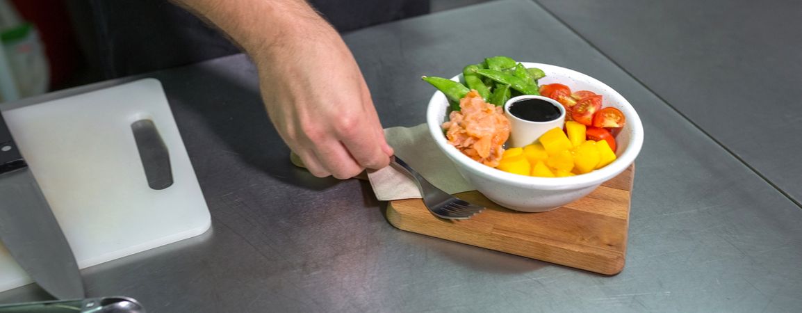 Banner of unrecognizable chef putting fork next to fresh poke bowl with salmon on restaurant kitchen