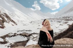 Back view of woman with pink headscarf sitting on a rock looking at snow-covered mountains 5nMAm0