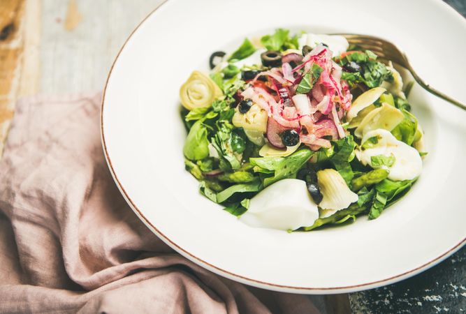 Close up of artichoke salad in bowl, on blue painted wooden background with linen napkin