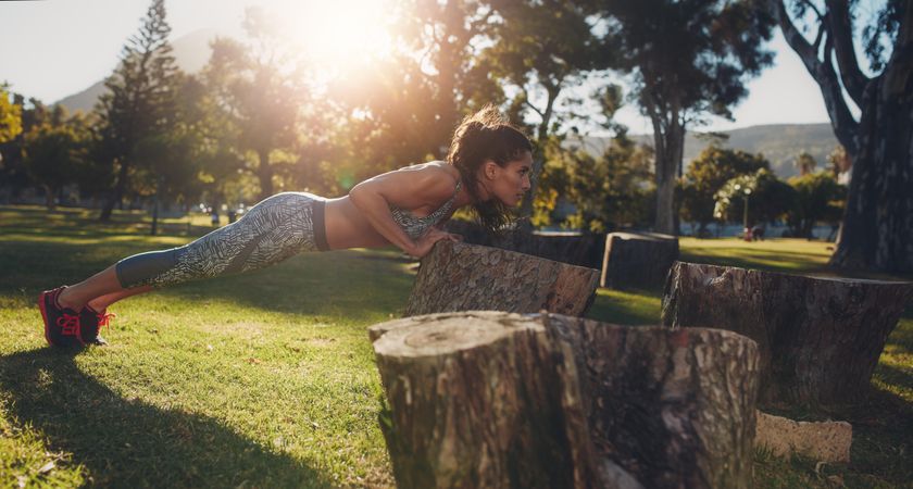 Tough young woman doing pushups on a log at park