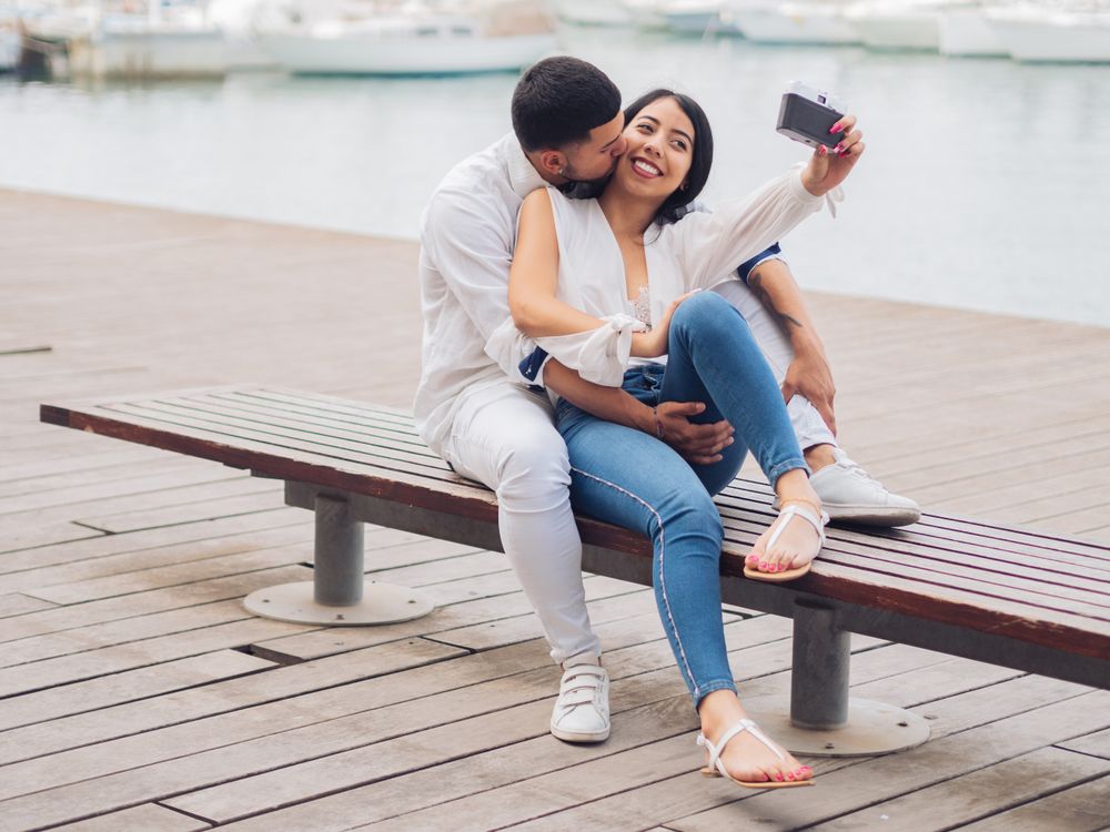 Woman with man taking photo selfie and kissing on bench