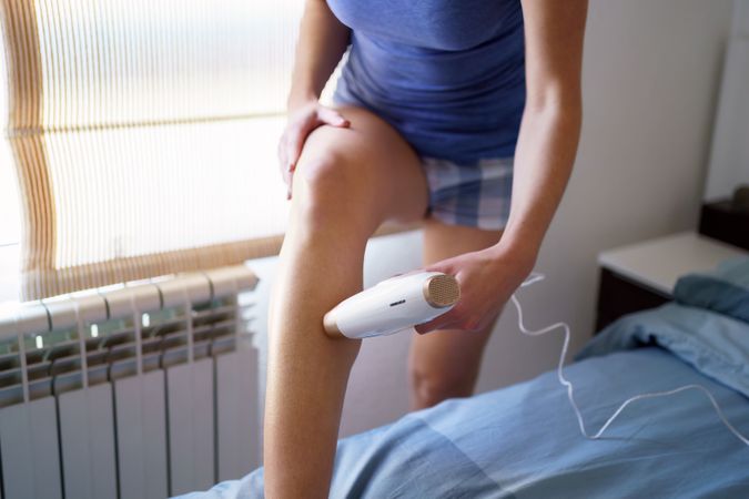 Cropped shot of woman standing in bedroom using hair removal laser