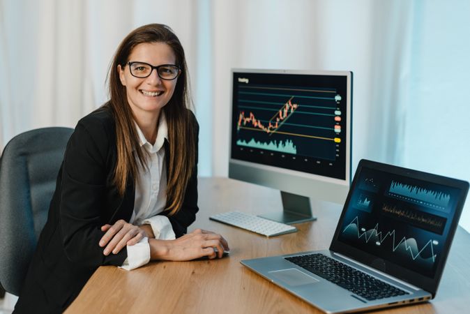 Female trader at table with laptop and computer monitor