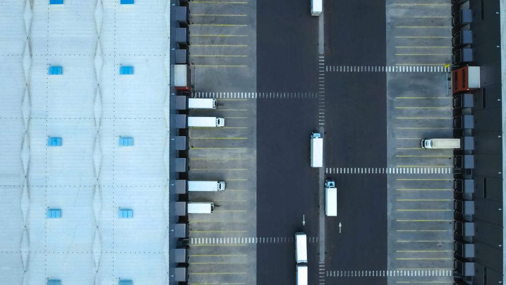 Aerial Side Shot of Industrial Warehouse Loading Dock where Many Truck with Semi Trailers Load
