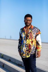 Black man wearing eyeglasses and loud shirt against blue sky while looking at camera