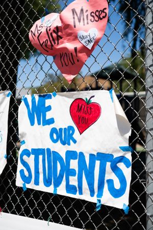 Two colorful signs taped to a school fence from teachers to students