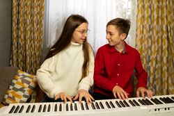 Girl and boy playing piano together while sharing joyful moment.