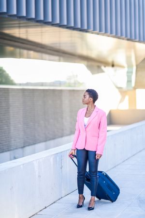Black woman with travel bag wearing pink jacket walking outside