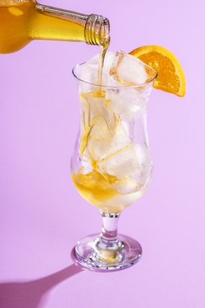Pouring orange liquid in a glass with ice cubes
