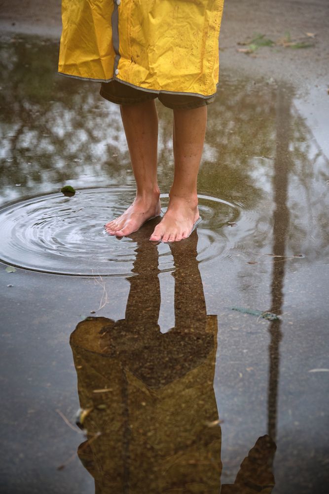 Unrecognizable child looking at reflection in puddle