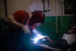 Side view of man in red protective helmet welding metal
