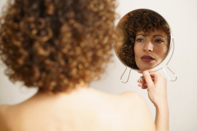 Back of woman looking into hand mirror