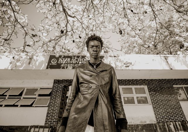 Grayscale photo of man in dark leather coat standing beside store front