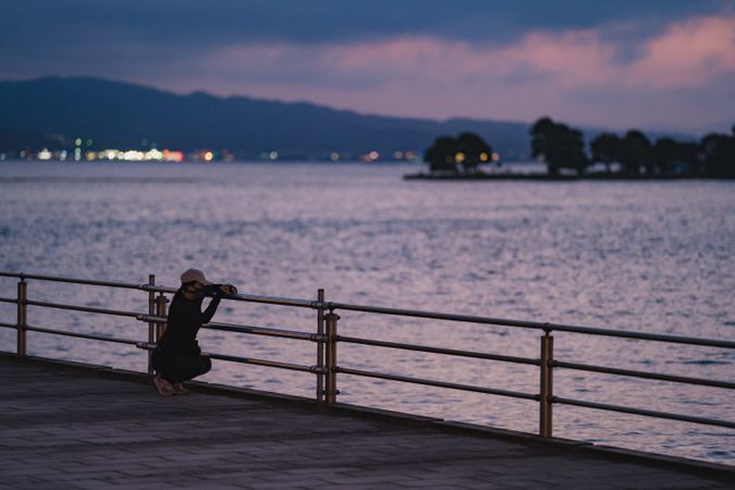 Person kneeling at pier looking out to the ocean
