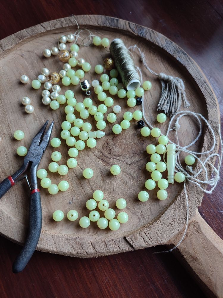 Green and pearly beads scattered on wooden board, along with strings and pliers