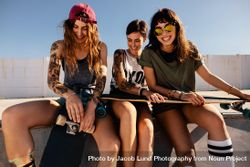 Three women skateboarders sitting together at the top of a skate ramp smiling 4dzNn0