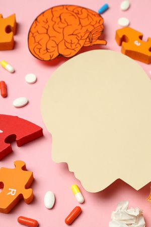 Vertical shot of paper cut out of side view of head with medications and puzzle pieces, close up