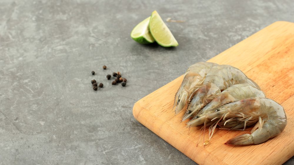 Uncooked prawns on board being prepared before cooking, with slices on lime and peppercorns
