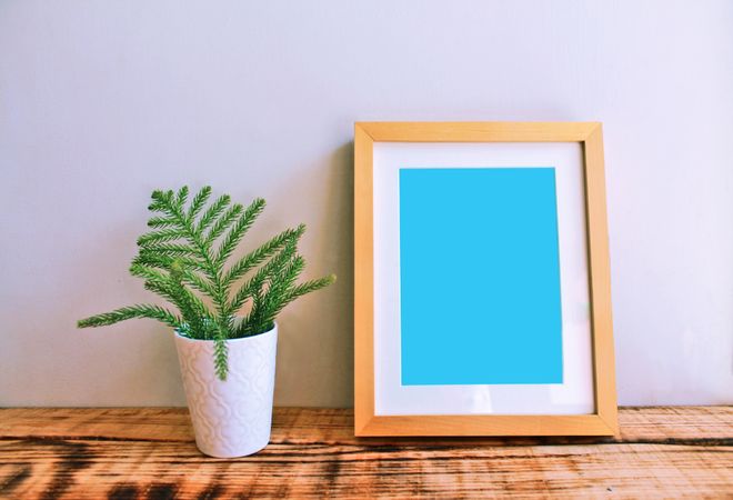 Wooden picture frame on desk with plant mockup