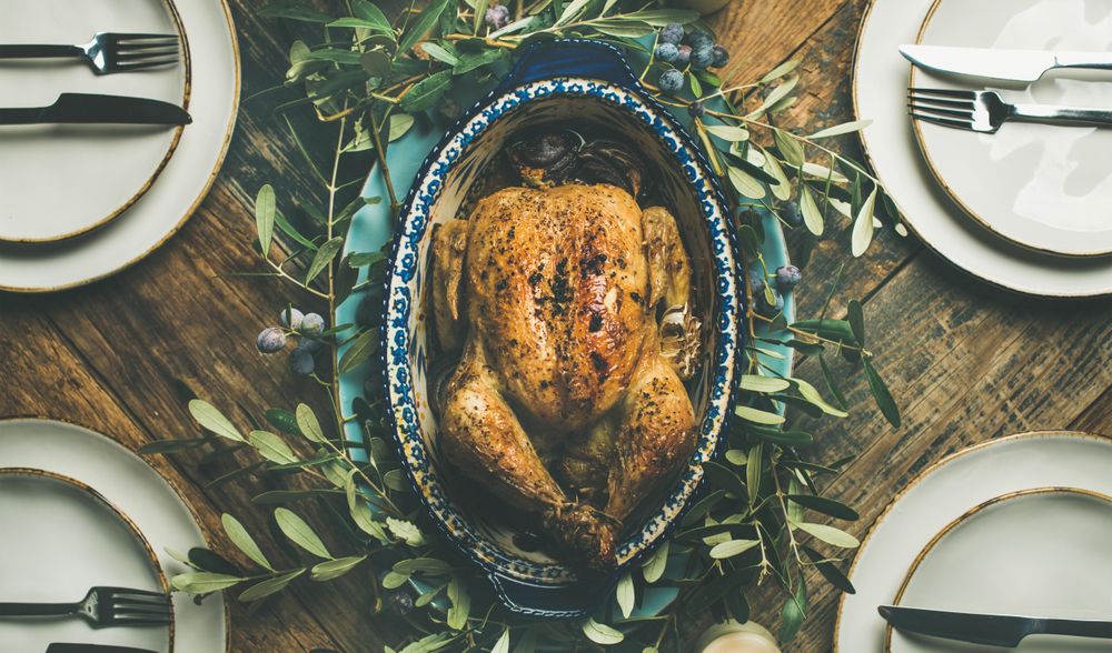 Top view of centerpiece of roast chicken with decorative branches, with four plate settings