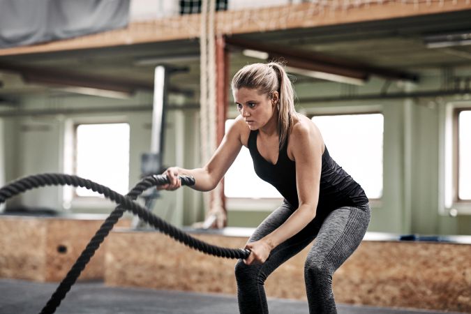 Healthy woman working out with ropes at gym