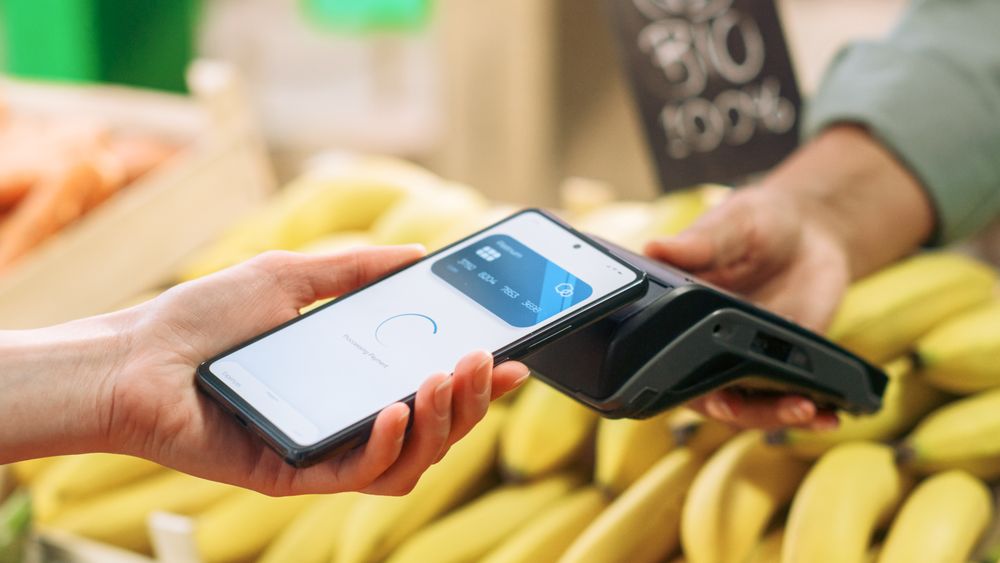 Close Up of a Customer Making a Secure Swift Contactless Payment Using a Smartphone with a Credit Card Banking App.