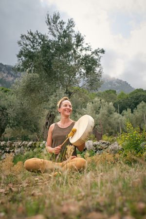 Cheerful woman playing tambourine during yoga in nature