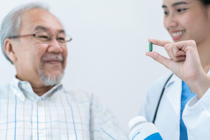 Older man smiling with medical professional holding pill for him
