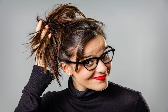 Woman with glasses and red lips touching her hair bun